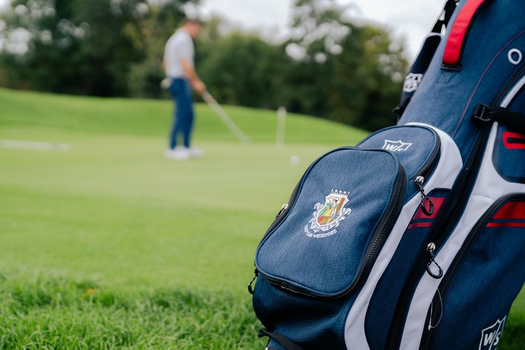 Golftasche mit Logo auf Rasen vor Golfer im Hintergrund