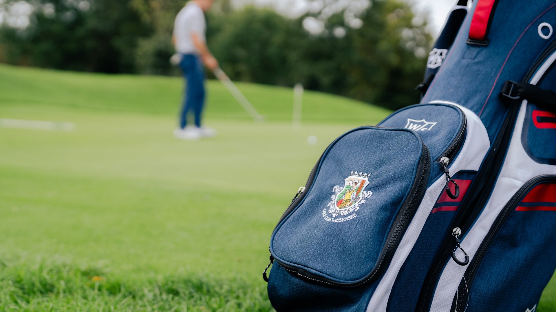 Golftasche mit Logo auf Rasen vor Golfer im Hintergrund