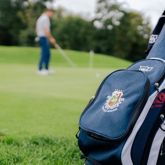Golftasche mit Logo auf Rasen vor Golfer im Hintergrund