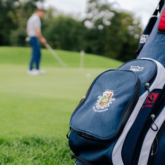 Golftasche mit Logo auf Rasen vor Golfer im Hintergrund