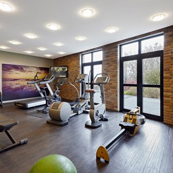 Moderner Fitnessraum mit Trainingsgeräten, Hanteln und großen Fenstern im Golf- & Sporthotel Wiesensee