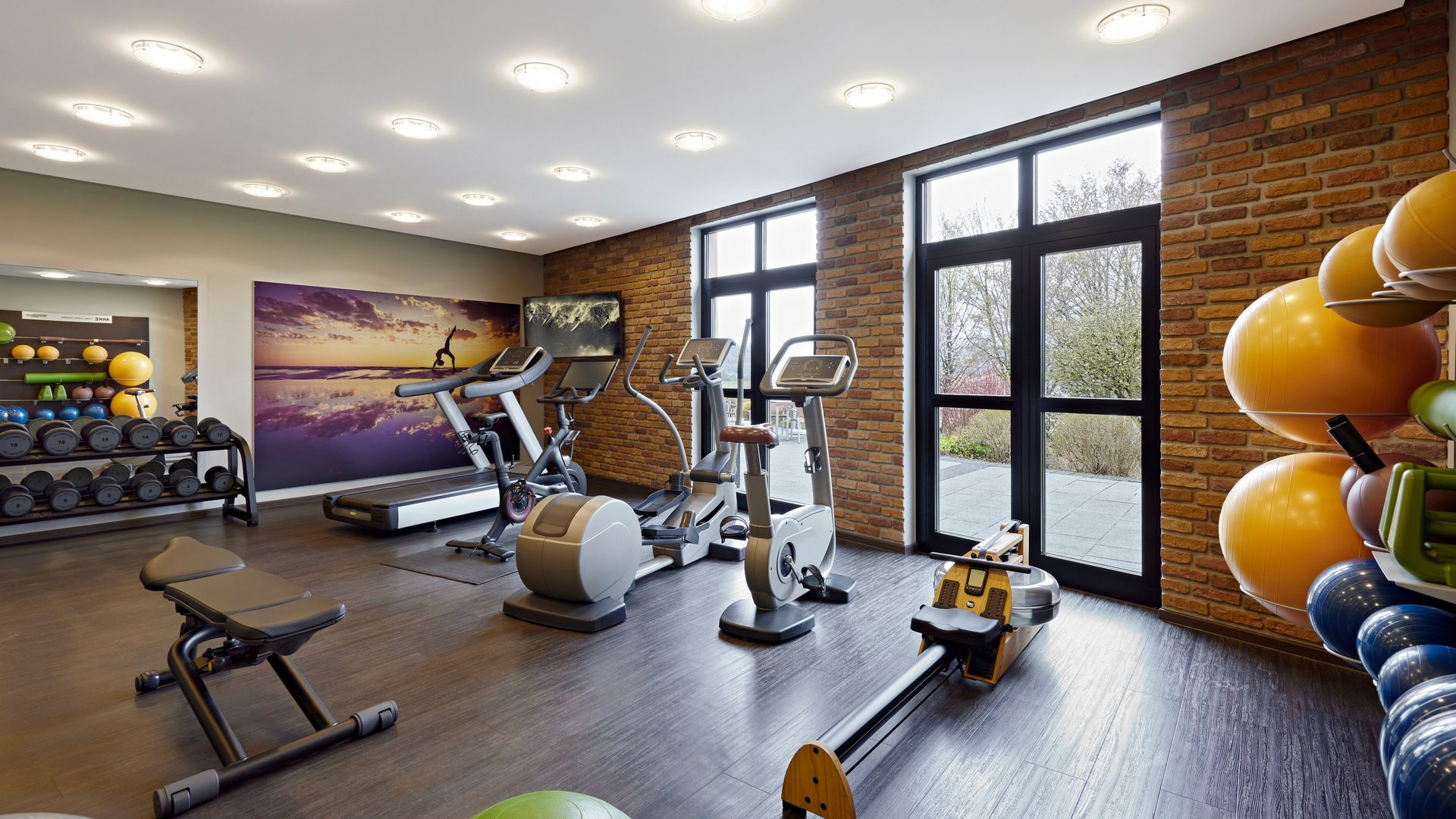 Moderner Fitnessraum mit Trainingsgeräten, Hanteln und großen Fenstern im Golf- & Sporthotel Wiesensee