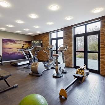 Moderner Fitnessraum mit Trainingsgeräten, Hanteln und großen Fenstern im Golf- & Sporthotel Wiesensee