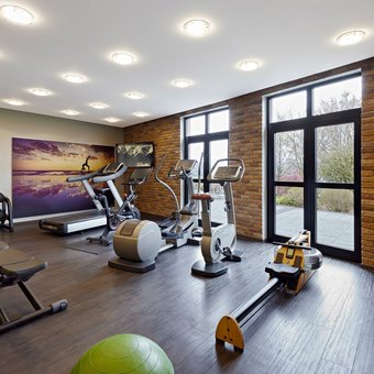 Moderner Fitnessraum mit Trainingsgeräten, Hanteln und großen Fenstern im Golf- & Sporthotel Wiesensee
