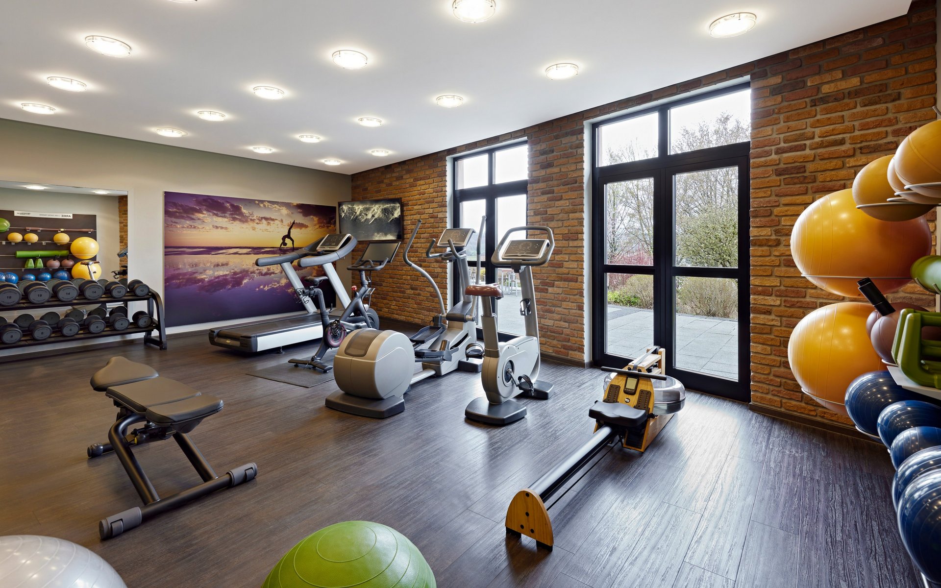 Moderner Fitnessraum mit Trainingsgeräten, Hanteln und großen Fenstern im Golf- & Sporthotel Wiesensee