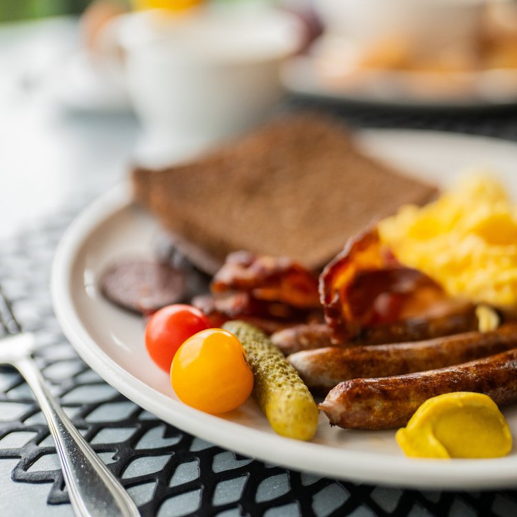 Herzhaftes Frühstück mit Rührei, Würstchen, Speck, Senf, Brot und frischem Gemüse im Golf- & Sporthotel Wiesensee